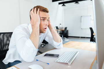 Shocked amazed young businessman using computer
