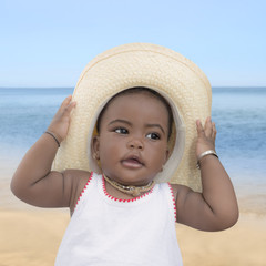 Baby girl wearing a straw hat at the beach, nine months old