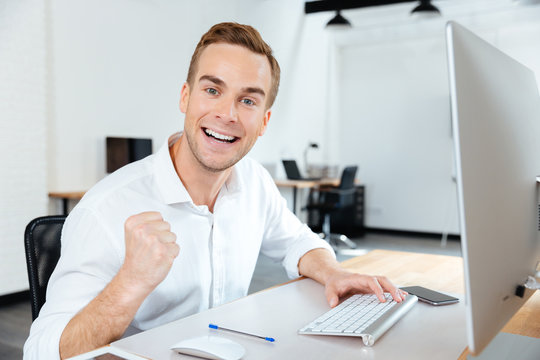 Cheerful successful young businessman celebrating success in office