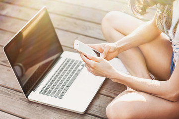 Fototapeta premium Young adult using smartphone and laptop outdoors