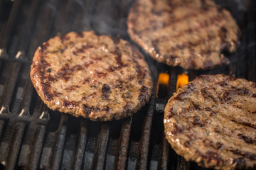 Drei Burger auf dem Grill. Rauch und Flammen sind zu sehen.