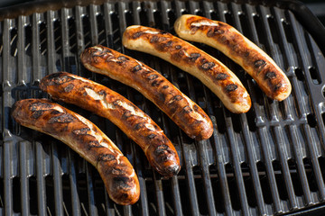 Fünf Grillwürste auf dem Grill. Von einer Seite fertig gegrillt.