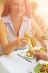 Close-up toned picture of red-haired woman smiling while sitting at table in restaurant or cafe with her husband. Happy people drinking white wine from glasses.