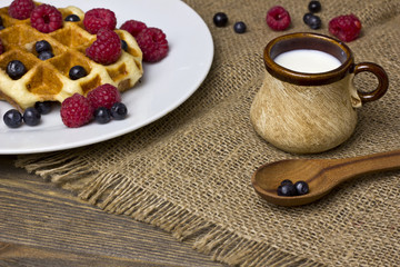 waffle with berries on a white plate. milk mug