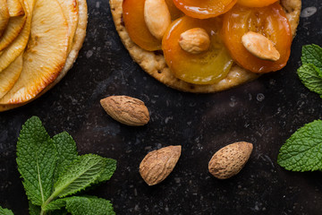 Tart with apricot and apple. Traditional french pie with fruits on dark marble background. Decorated almonds and mint leafs. Delicious dessert with copy space closeup.
