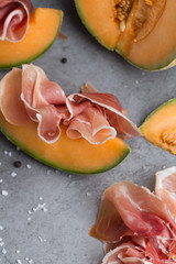 Jambon mix. Ham. Traditional Italian and Spanish salting, smoking, dry-cured dish - jamon Serrano and prosciutto crudo sliced with melon on grey background. Copy space. Closeup. 
