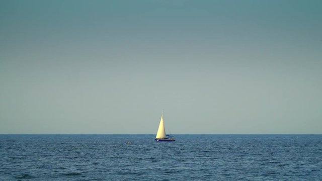 The yacht with sails floating on the sea. Against the background of the blue sky