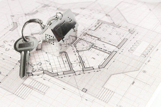 key with keychain in the form of a silver-colored house on a background of architectural drawing