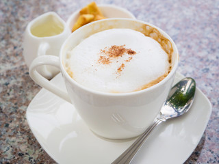 White cup of cappuccino stands on the rock table, selective focus