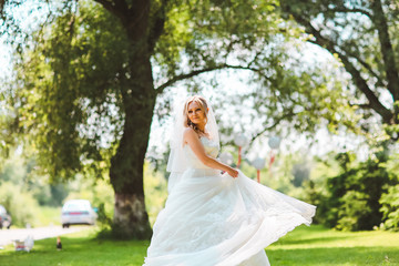 Fototapeta na wymiar Beautiful romantic stylish blonde bride in white dress dancing in the forest in the sun. Summer meadow park. Woman turn around in white dress.