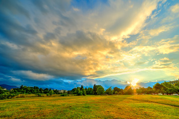 Naklejka premium Beautiful background landscape at sunset time, with colorful clouds on sky illuminated by sun, in summer season