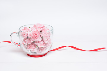 Glass cup full of pink roses with red ribbon around it on white