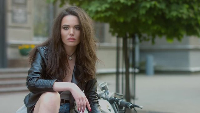 4K CINEMAGRAPH - motion photo seamless loop - Beautiful girl in leather jacket sitting on the custom motorcycle in the street. 60 FPS 4K UHD