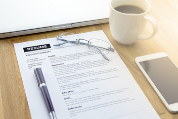 Businessman or job seeker review his resume on his desk before send to finding a new job with pen, computer laptop, glasses, a cup of coffee and smart phone.