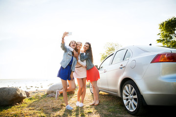 happy women taking selfie near car at seaside