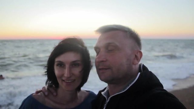 Happy couple taking selfie on beach at sunset using phone
