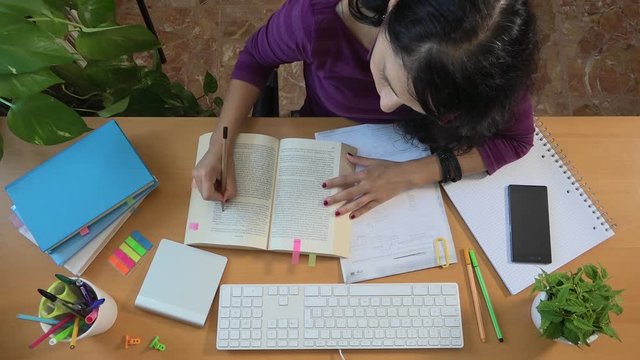 Female college student studying to preparing exam and putting page marker. Caucasian girl reading a book and writing notes. Studying for degree. Young people, university life and learning