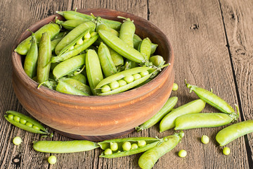  Green peas.  Pods of green peas in a wooden bowl on a brown wooden floor.