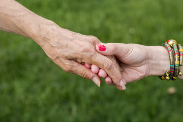 Old and young woman holding hands on green background, closeup