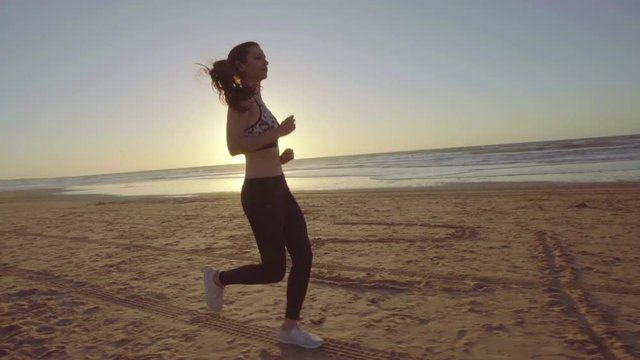 Chica joven corriendo en camara lenta al atardecer en la playa