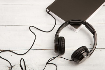 Audio book concept with black book and headphones on white wooden background