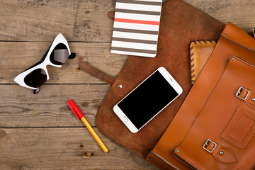women set with bag, smart phone, sunglasses, notepad, pen and purse on brown wooden desk