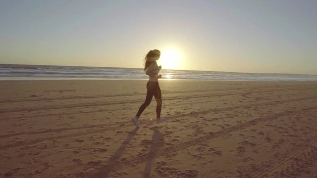 Chica joven corriendo en camara lenta al atardecer en la playa