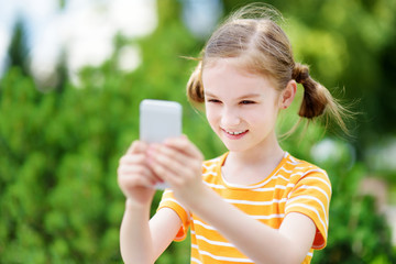 Cute little girl playing outdoor mobile game on her smart phone