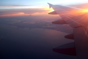 Rays of light in twilight sunset purple orange sky view from window airplane, fly over the ocean at evening time