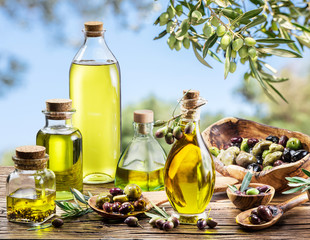 Bottles of olive oil on the old wooden table under olive tree.