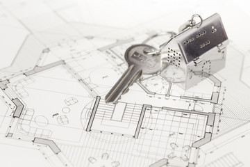 key with keychain in the form of a silver-colored house on a background of architectural drawing