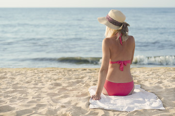 Woman in a pink bathing suit on the beach looking at the sea