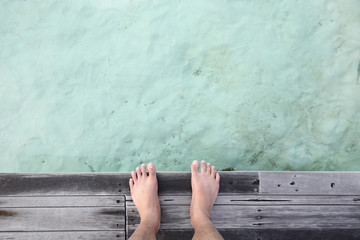 male feet standing on a wooden pier against a beautiful blue sea