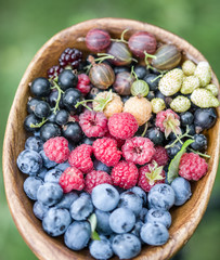 Ripe berries in the wooden bowl over green grass.