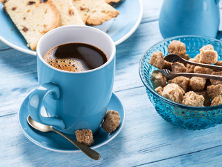 Cup of coffee, milk jug, cane sugar cubes and fruit-cake.
