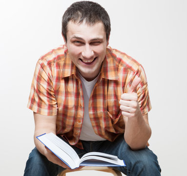 Happy young man holding a book and showing a thumb up sign