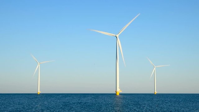 Wind turbines with rotating blades in an offshore wind park during a beautiful summer day.