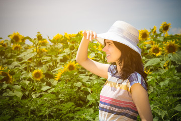 Side view portrait of young female wearing hat in the sunflower field during the summer day. Summer season, retro and fashion concepts. 