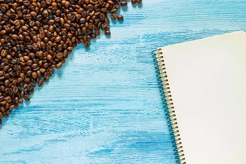 Single simple empty white notebook with a blank for drawing or writing, scattered roasted coffee beans are on a Desktop from blue wooden plank. Top view. Mock up. Flat lay