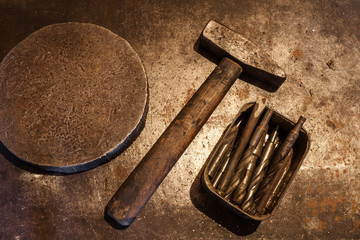 The old steel hammer with wooden handle, iron heavy ring and drill bits for metal in the box on the...