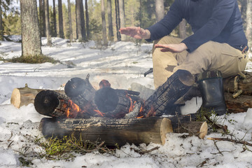 man warming his hands around a campfire in the forest