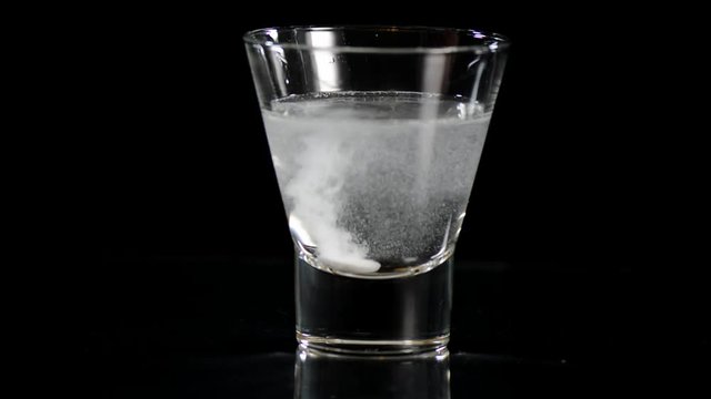 Dissolving two pain killer preparation tablets in glass of water against a black background.