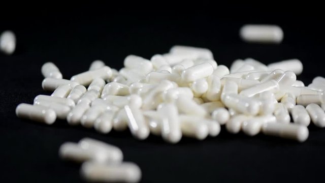 Falling white capsules on black background, close up, with womans hand.