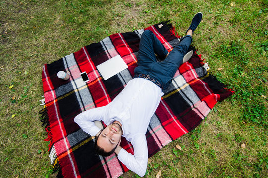 Happy young man with laptop relaxing on the grass, view from the top