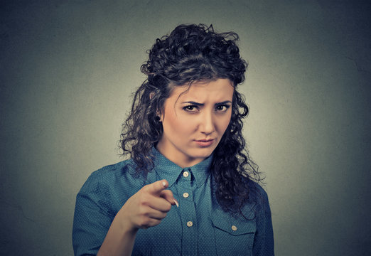 angry young woman pointing at camera isolated on gray background