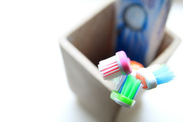 Fototapeta na wymiar Shallow DOF shot of three toothbrushes and toothpaste in a clay tumbler in the morning light