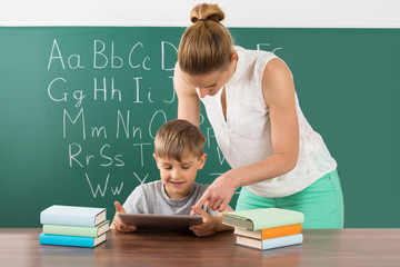 Teacher With Boy Using Digital Tablet In Classroom