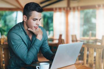 Young man sitting at cafe and working on laptop