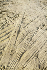 Many tire tracks and footprints in different directions on the beach sand. Tyre traces texture background