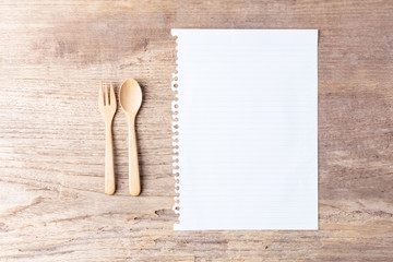 Close up wooden spoon, fork and blank paper on wooden table top